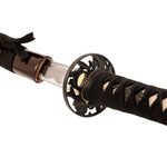 A close-up of the SMAI High Carbon Steel Katana - Crimson Eclipse, featuring a black wrapped handle, ornate handguard, and partially drawn shiny blade with the scabbard visible in the background.
