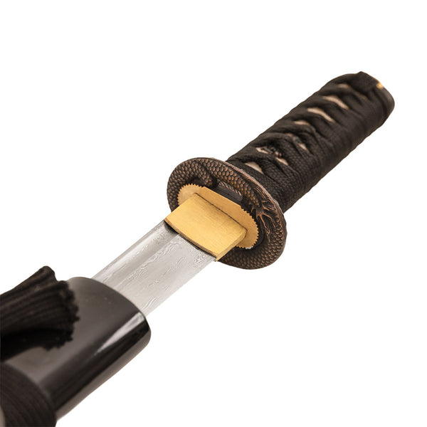 A close-up of the SMAI Damascus Black Infinite Dragon Tanto, showing its full tang construction, black cord-wrapped handle, partially drawn blade from a black scabbard, and a decorative brass guard.