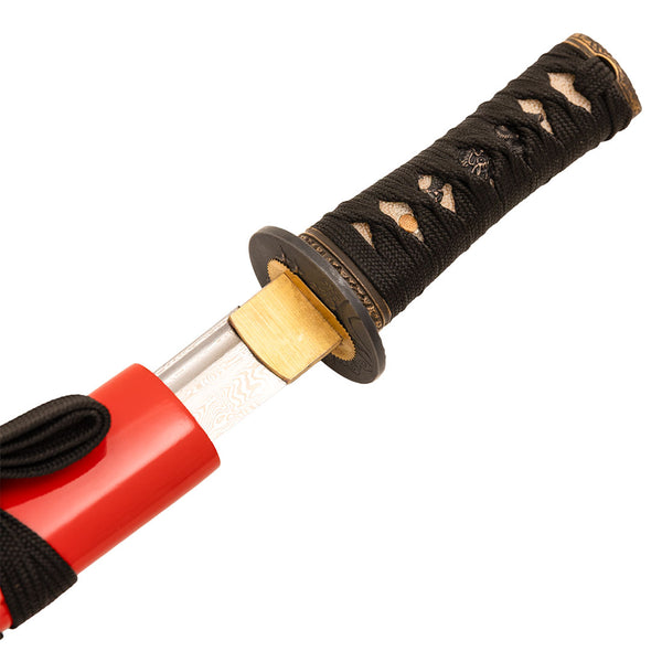 Close-up of the SMAI Damascus Red Tiger Tanto, partially sheathed in a red scabbard, highlighting its black handle with gold accents and detailed guard on this full tang blade.