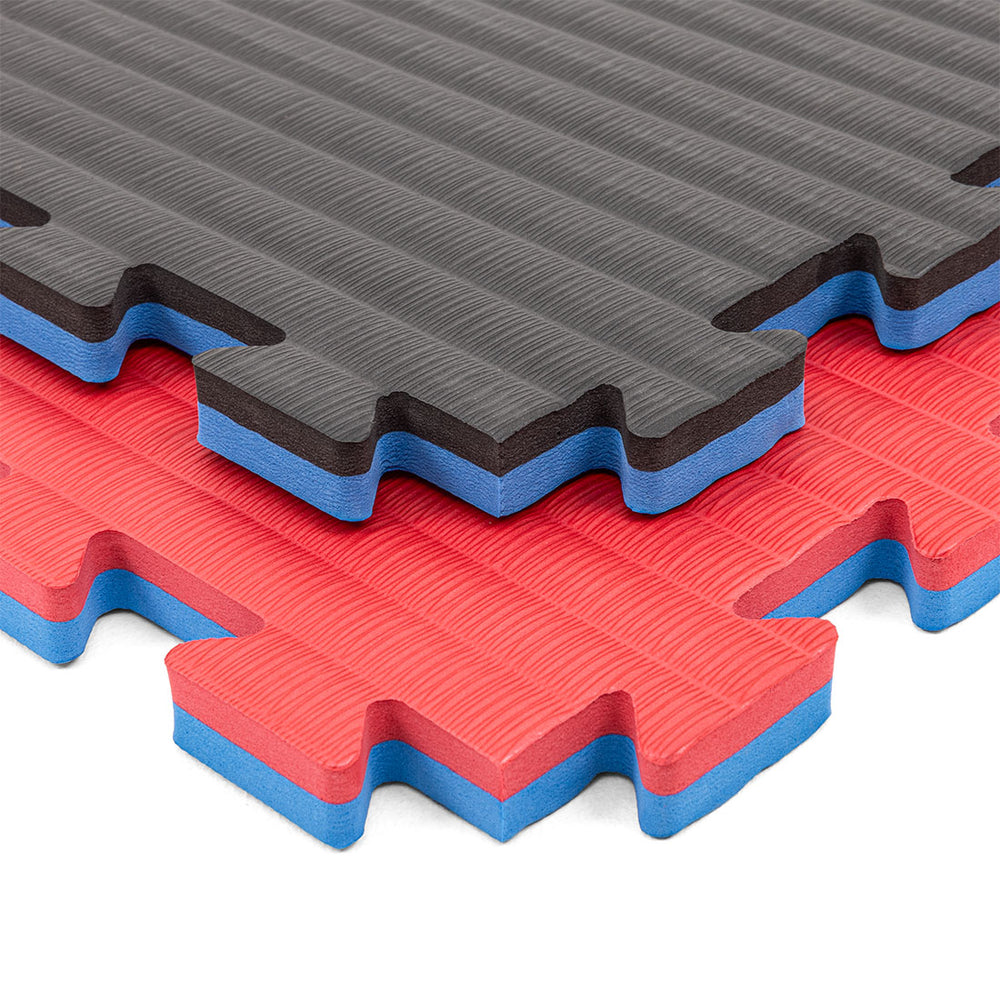 Three SMAI Jigsaw Mats - 2cm - Factory Seconds - are stacked: the top mat is gray and black, the middle red and blue, and the bottom red and blue. Each features textured surfaces and puzzle edges for easy connection.