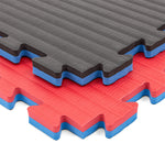 Three SMAI Jigsaw Mats - 2cm - Factory Seconds - are stacked: the top mat is gray and black, the middle red and blue, and the bottom red and blue. Each features textured surfaces and puzzle edges for easy connection.