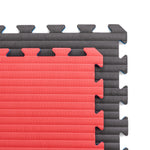Two interlocking SMAI Jigsaw Mats (2cm, Factory Seconds with cosmetic imperfections) in red and black are partially connected. The ribbed, textured mats have zigzag edges that fit together like puzzle pieces. Top view shown.