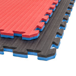 Three interlocking SMAI Jigsaw Mats (2cm, Factory Seconds) are stacked: the top is red, others black. These EVA mats have blue sides, textured grooves, and zigzag edges—ideal gym tiles with cosmetic imperfections.
