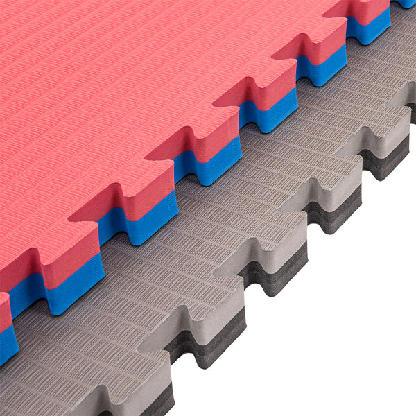 Four SMAI Jigsaw Mats (4cm, Factory Seconds with cosmetic imperfections) are stacked diagonally; the top two tiles are red with blue edges and the bottom two are gray with black edges. All mats have textured surfaces and puzzle-like edges.