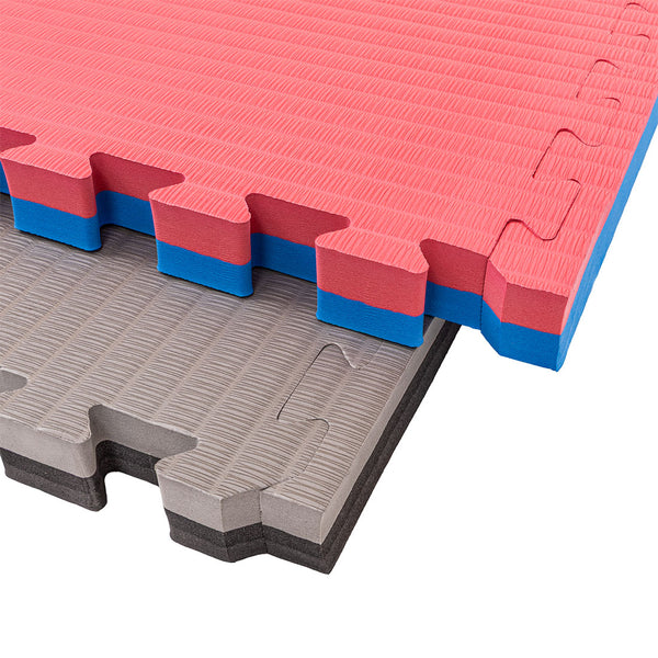 Two SMAI Jigsaw Mat - 4cm - Factory Seconds (with cosmetic imperfections) are stacked: a red/blue mat on top and a gray/black one below. Both have textured surfaces and puzzle edges—ideal for home workouts.