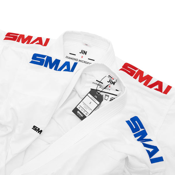 Two white WKF Karate Uniforms (8oz Premium Kumite Gi - Jin) by SMAI, each with red and blue “SMAI” on the shoulders, labels and tags on the collars showing size and brand—ideal for competition use.