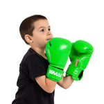 A boy in a black shirt wears SMAI Essentials Kids Boxing Glove - Green, holding his fists up near his face and looking slightly upward against a plain white background.