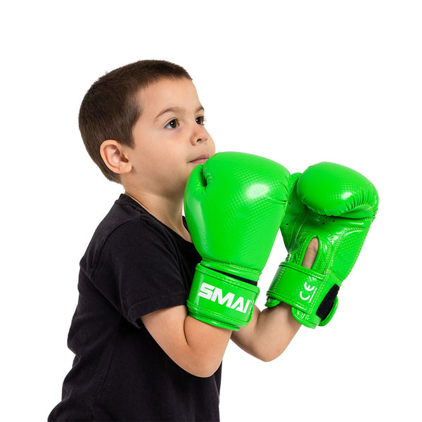 A boy in a black shirt wears SMAI Essentials Kids Boxing Glove - Green, holding his fists up near his face and looking slightly upward against a plain white background.