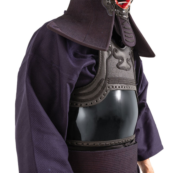 A person wears the SMAI Kendo Bogu Set, featuring a deep blue robe and black chest protector, with parts of the helmet and neck guard visible. The face is partially obscured by the traditional training protection gear.