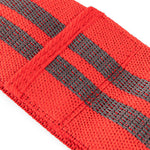 A close-up shot features a red knitted mini resistance band from the No Sync To Channel Engine's set of three, adorned with two parallel black stripes. Its coarse texture reveals a woven pattern. The sharp focus on the foreground highlights the band’s intricate details, making it ideal for glute activation, while the softly blurred background enhances its prominence.
