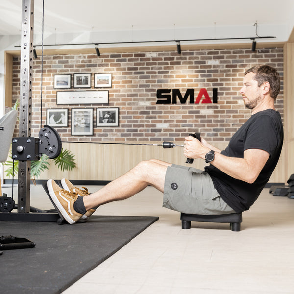 A man sits on a SMAI Low Row Seat Floor using a cable rowing machine.