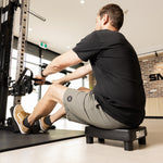 A person seated on an SMAI Low Row Seat Floor while using a cable row machine.