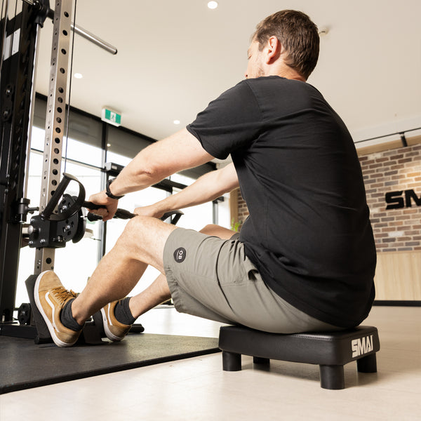 A person seated on an SMAI Low Row Seat Floor while using a cable row machine.