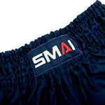 Close-up of SMAI Muay Thai Shorts - Navy, crafted from satin and designed with an elastic waistband, featuring a stitched rectangular SMAI brand patch with a red “A” and white lettering.