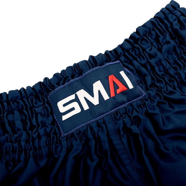Close-up of SMAI Muay Thai Shorts - Navy, crafted from satin and designed with an elastic waistband, featuring a stitched rectangular SMAI brand patch with a red “A” and white lettering.
