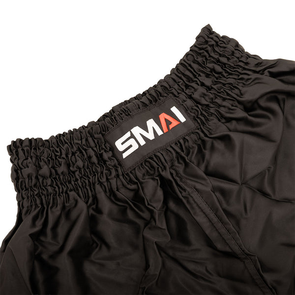 Close-up of the waistband of SMAI Muay Thai Shorts - Black, featuring a gathered elastic band and a sewn-on SMAI label in white and red letters.