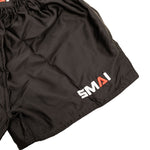 The SMAI Muay Thai Shorts - Black feature an elastic waistband, smooth satin polyester fabric, and white/red "SMAI" embroidery on the lower left leg for a classic athletic look.