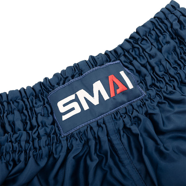Close-up of the waistband on SMAI Muay Thai Shorts - Navy, showing the gathered elastic design and a sewn-on rectangular patch with the SMAI logo in white and red.