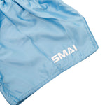 SMAI Muay Thai Shorts - Sky Blue, crafted from smooth, slightly shiny satin polyester with "SMAI" embroidered in white on the lower hem. Unisex design.