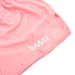 SMAI Muay Thai Shorts - Pink: Light pink satin polyester with "SMAI" white embroidery on the lower leg, shown in a close-up highlighting the fabric and stitching details.