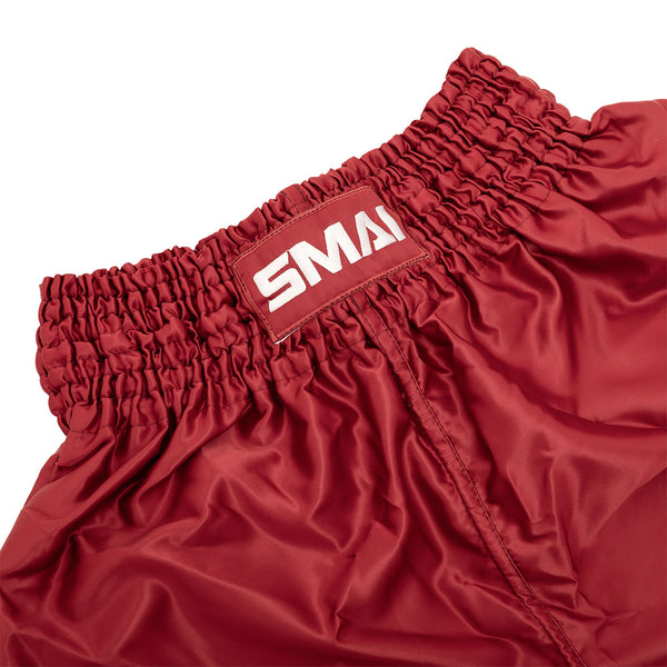 Close-up of the waistband on SMAI’s Muay Thai Shorts - Red, showing shiny, quick-dry satin fabric, a gathered elastic band, and a rectangular patch with partially visible white "SMAI" text.