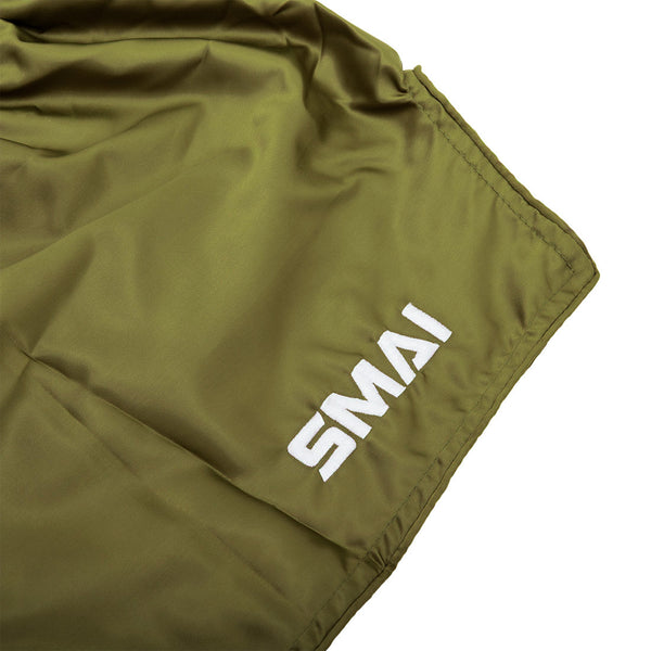 A close-up of SMAI’s Muay Thai Shorts in olive green Satin Polyester, showcasing the white "SMAI" embroidery in the corner and the slightly wrinkled unisex fabric.