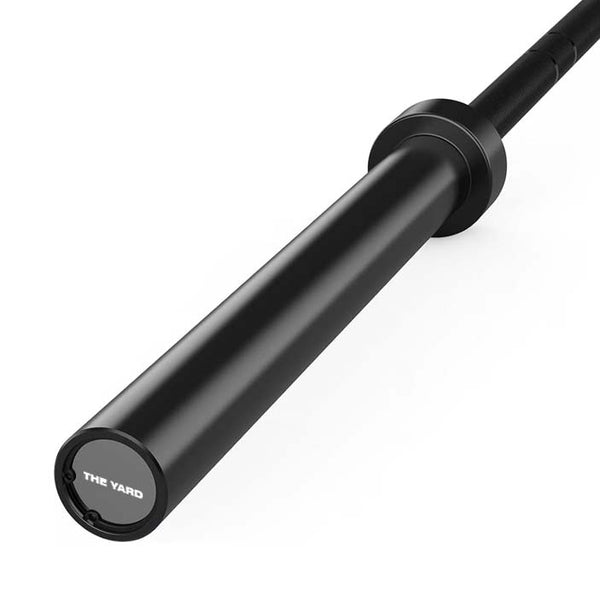A close-up of the SMAI The Yard - Barbell - 20kg - Black, featuring "THE YARD" logo on the end cap, photographed against a white background.