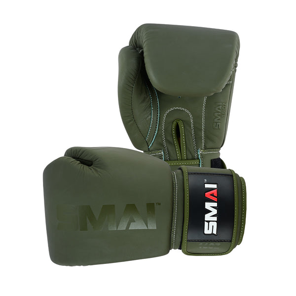 The SMAI Elite85 Boxing Glove in olive green features visible stitching and a black and white SMAI logo on the wrist strap. Designed to reduce injury, one glove stands upright while the other lies on its side.