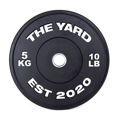 The SMAI The Yard - HD Bumper Plate (Pair) 5kg features a black design with "THE YARD" at the top, "5 KG" left, "10 LB" right, and "EST 2020" below, plus a silver center—ideal for Olympic or CrossFit training.