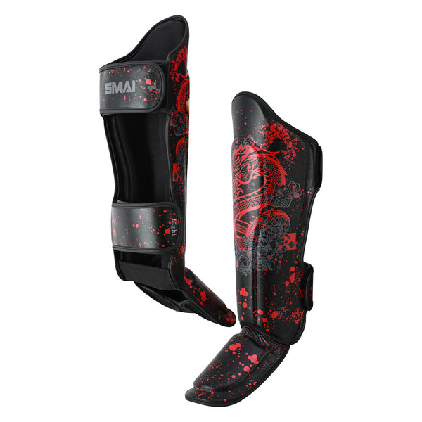 The SMAI Muay Thai Shin Instep Guard - Black Dragon features red splatter and dragon designs on durable synthetic leather, with adjustable straps and thick padding for protection—shown upright against a white background.
