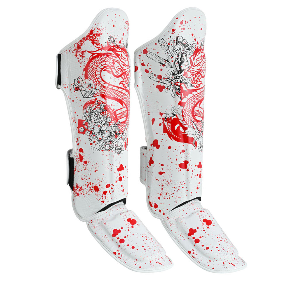 The SMAI Muay Thai Shin Instep Guard - White Dragon features white EVA foam protection, red splatter patterns, red dragon illustrations, and black floral designs. The pair stands upright against a white background.