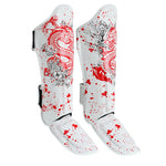 The SMAI Muay Thai Shin Instep Guard - White Dragon features white EVA foam protection, red splatter patterns, red dragon illustrations, and black floral designs. The pair stands upright against a white background.