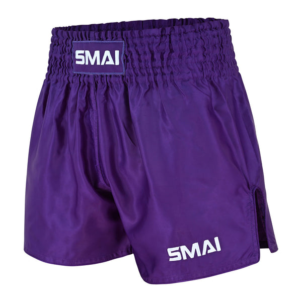 SMAI Muay Thai Shorts - Purple feature a wide elastic waistband for a comfortable unisex fit, with “SMAI” displayed on both the front waistband patch and left leg. These shorts offer side slits for enhanced movement and have a shiny fabric finish.