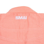 Close-up of the back collar of the SMAI Supreme X Brazilian Jiu Jitsu Uniform in salmon, featuring white embroidery and stitching on a textured pearl weave—perfect as a youth BJJ gi.