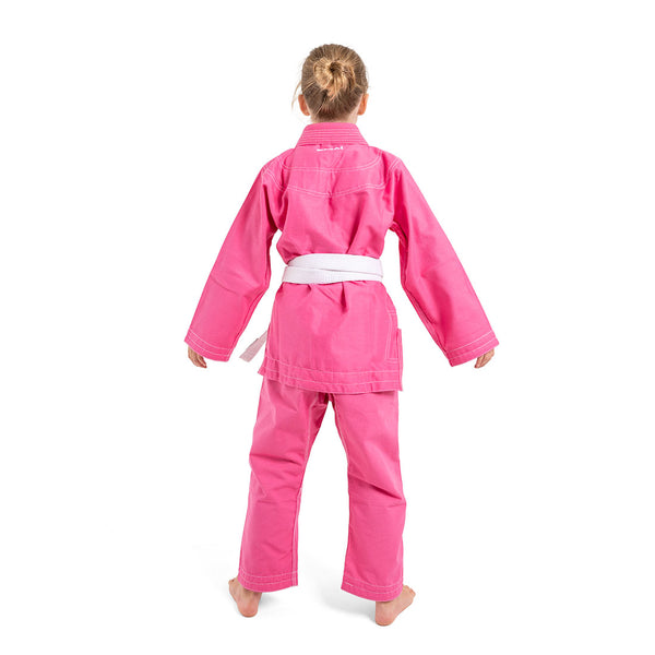 A young child stands barefoot facing away in an SMAI Supreme X Brazilian Jiu Jitsu Uniform in pink with a white belt, set against a plain white background.