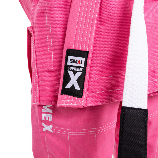Close-up of the SMAI Supreme X Brazilian Jiu Jitsu Uniform in pink, featuring a black and white "SMAI SUPREME X" patch on the jacket, "SUPREME X" embroidery on the pants, durable Rip Stop fabric, and a matching white & black belt.