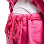 Close-up of a person wearing the SMAI Supreme X Brazilian Jiu Jitsu Uniform in pink, featuring durable pearl weave pants with a drawstring waist, tied over a white shirt to showcase the texture and detailed stitching.