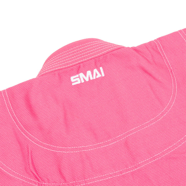 A close-up of the Supreme X Brazilian Jiu Jitsu Uniform in pink by SMAI, made from durable Rip Stop fabric with white stitching and the "SMAI" logo embroidered in white near the collar.