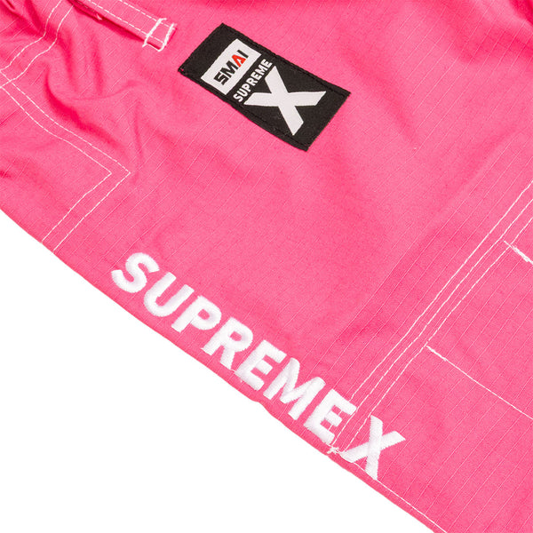 Close-up of the SMAI Supreme X Brazilian Jiu Jitsu Uniform in pink, crafted from durable ripstop fabric with white stitching, a black "SMAI SUPREMEX" patch, and bold "SUPREMEX" lettering along the gi.