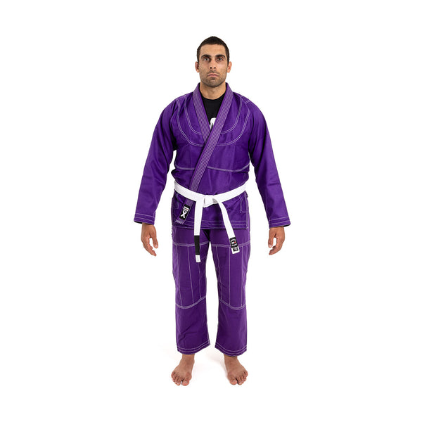A person stands barefoot on a white background, facing forward with arms relaxed, wearing the SMAI Supreme X Brazilian Jiu Jitsu Uniform in purple and a white belt.