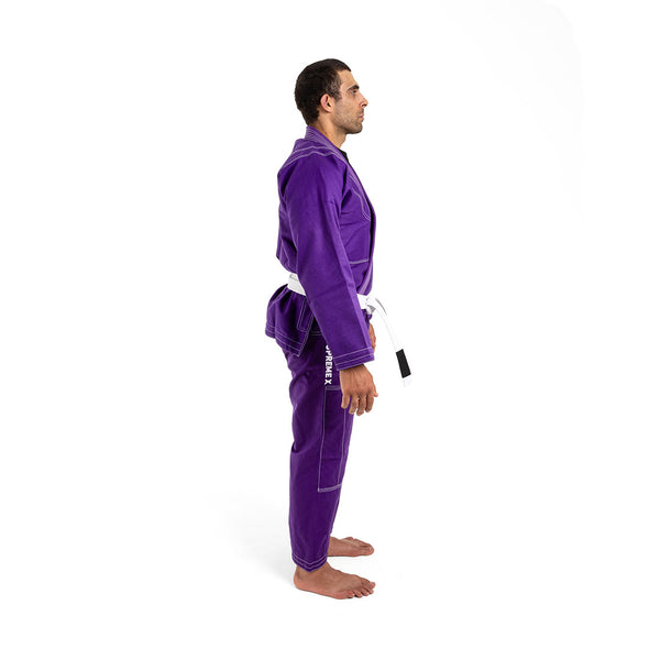 A man, barefoot and in profile, wears the SMAI Supreme X Brazilian Jiu Jitsu Uniform in purple with reinforced stitching and a white belt, set against a plain white background.