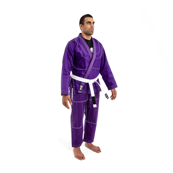 A man stands barefoot on a white background, wearing the SMAI Supreme X Brazilian Jiu Jitsu Uniform in purple with reinforced stitching and a white belt, facing slightly to the side with arms relaxed at his sides.