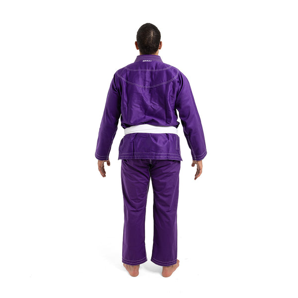 A person stands barefoot, facing away from the camera, wearing an SMAI Supreme X Brazilian Jiu Jitsu Uniform in purple with reinforced stitching and a white belt, set against a plain white background.