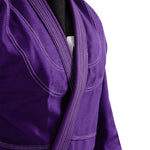 A close-up of a person wearing the SMAI Supreme X Brazilian Jiu Jitsu Uniform in textured purple pearl weave with reinforced stitching, shown from shoulders to waist against a white background.