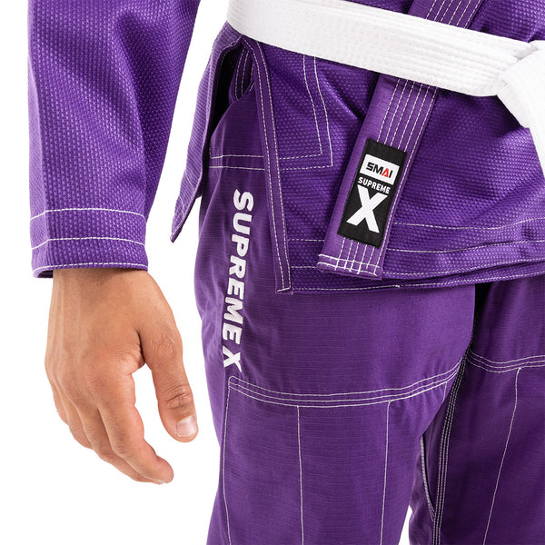 A person wears the SMAI Supreme X Brazilian Jiu Jitsu Uniform in purple, featuring white stitching, a white belt, "SUPREMEX" on the rip stop pants, and a "SMAI SUPREME X" label near the belt. Only the lower torso and one arm are visible.