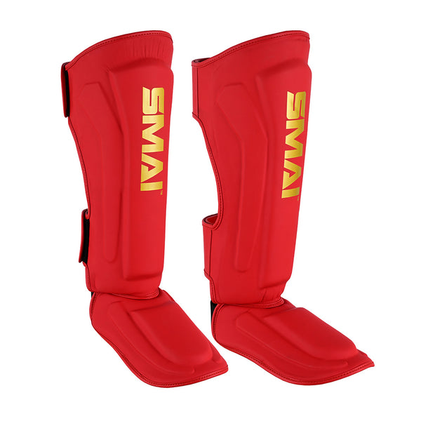 A pair of SMAI Gold Series Muay Thai Shin Guards in red/gold, featuring yellow "SMAI" branding and multi-layer EVA protection, shown upright with attached foot protectors for martial arts.