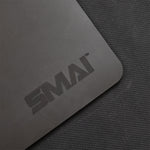 A close-up of the SMAI Pilates Reformer Carriage Topper / Protector, a gray rectangular mat with “SMAI” printed in dark letters, shown on a textured dark gray fabric surface.