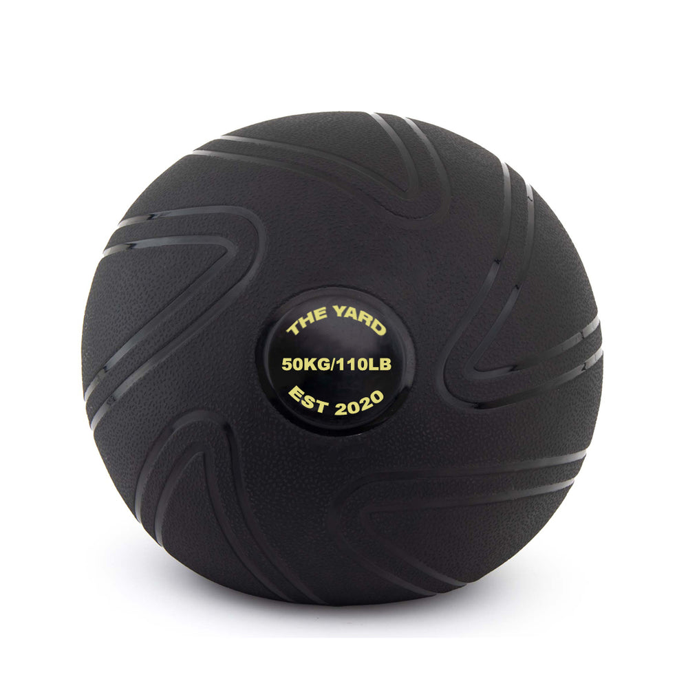 The Yard - Slam Ball 50kg by SMAI is a black, sand-filled rubber ball with textured grooves. The center label features "THE YARD 50KG/110LB EST 2020" in yellow text.
