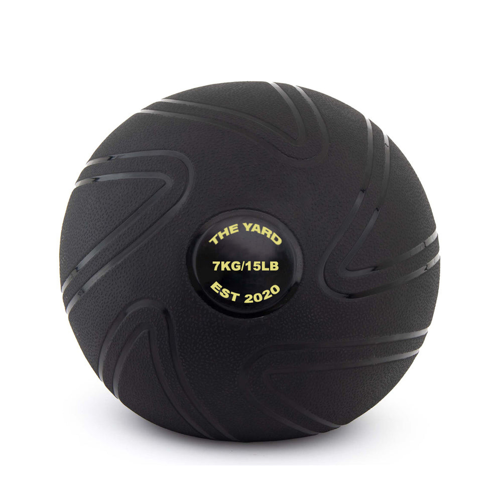 The SMAI The Yard - Slam Ball 7kg is a black rubber ball with a textured, grooved surface. Its center label displays “THE YARD 7KG/15LB EST 2020” in yellow. The ball stands upright against a white background.