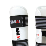 Close-up of a pair of white Taekwondo forearm guards with black straps, showcasing the partial logo "SMAI" on the front. The design includes carbon fiber style detailing, and a small red "M" indicates the size on the inner lining.